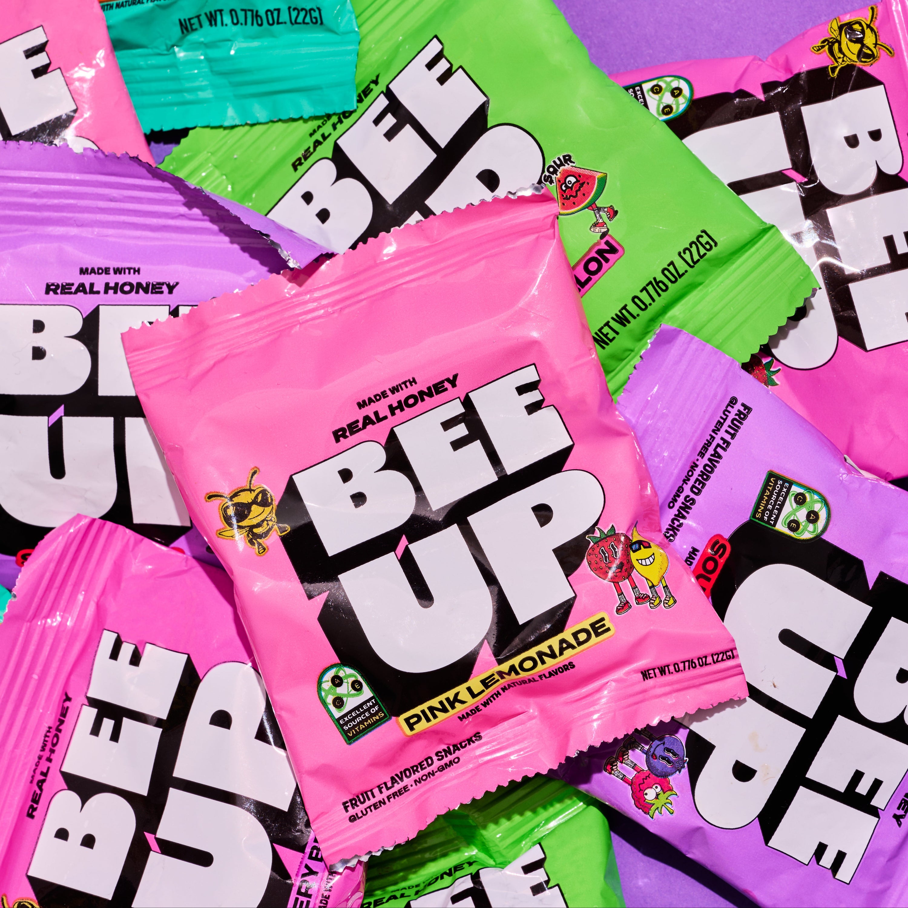 Scattered BEEUP individual snack pouches in pink, green, and purple flavors including Pink Lemonade and Tropical Mix, featuring Becks mascot