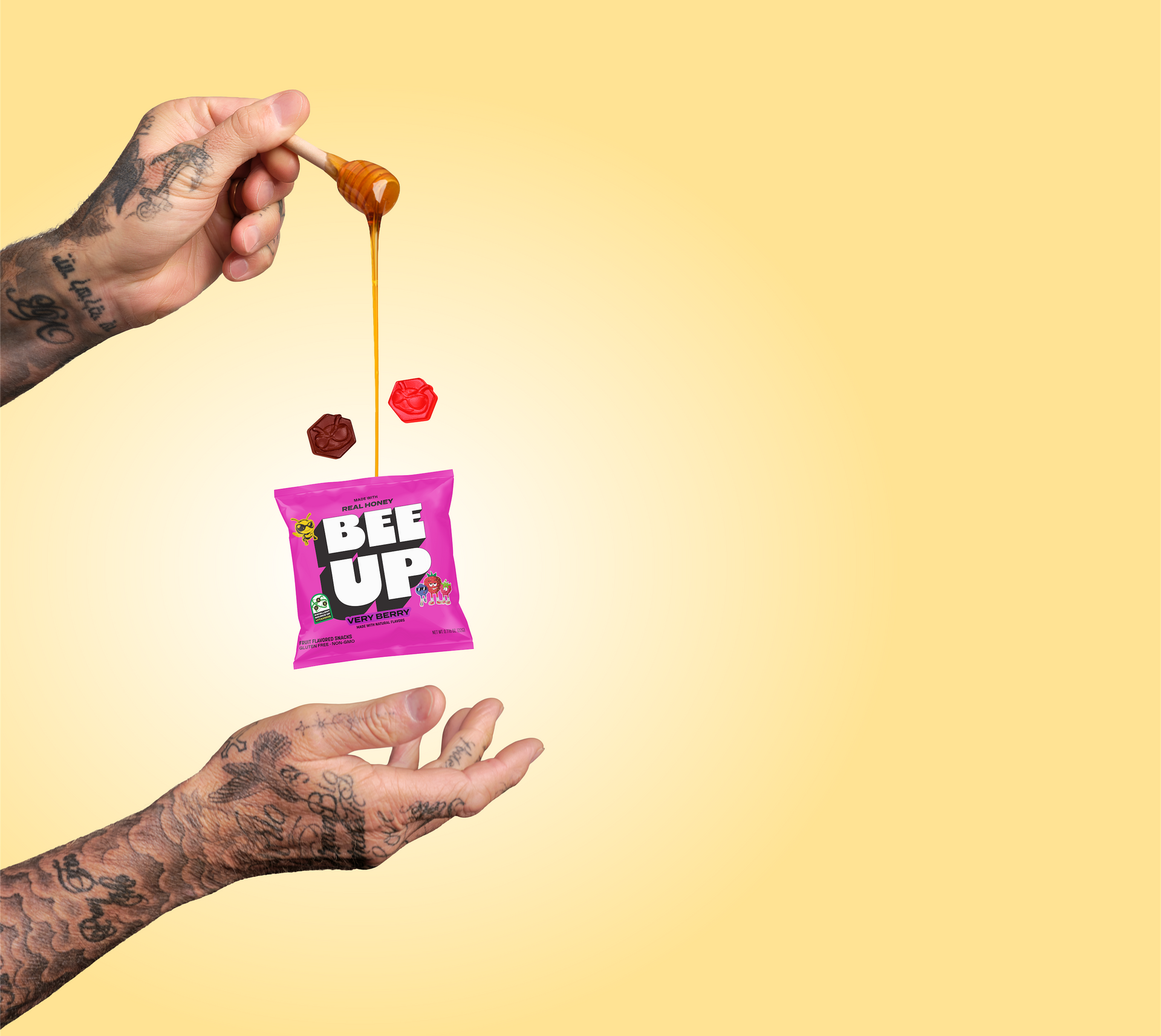 David Beckham's hands, holding a magenta pouch of "Very Berry" BEEUP honey fruit snacks and honey dipper, drizzling honey into the pouch over a light yellow background. There are two gummies floating in between, one red and the other purple.