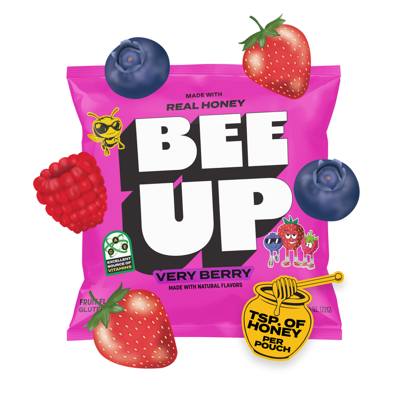A magenta pouch of "Very Berry" BEEUP  honey fruit snacks surrounded by blueberries, strawberries, raspberries and a honey jar & dipper sticker