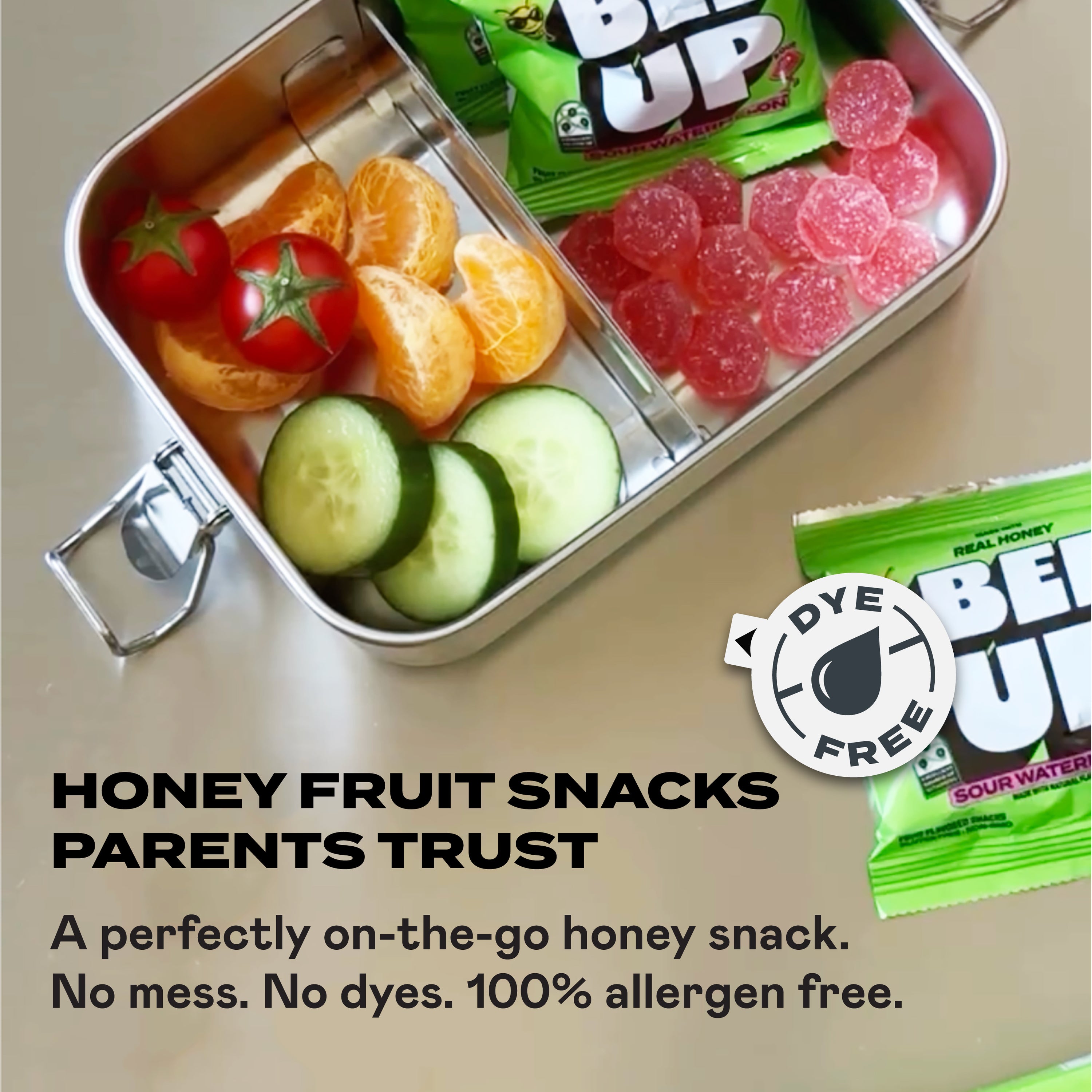 Metal lunchbox with two pouches of sour watermelon BEEUP honey fruit snacks, fruits and vegetables on a neutral background. Sticker overlay states, "Dye Free"
Text on the bottom says, "Honey fruit snacks parents trust. A perfectly on-the-go honey snack. No mess, No Dyes. 100% allergen free"